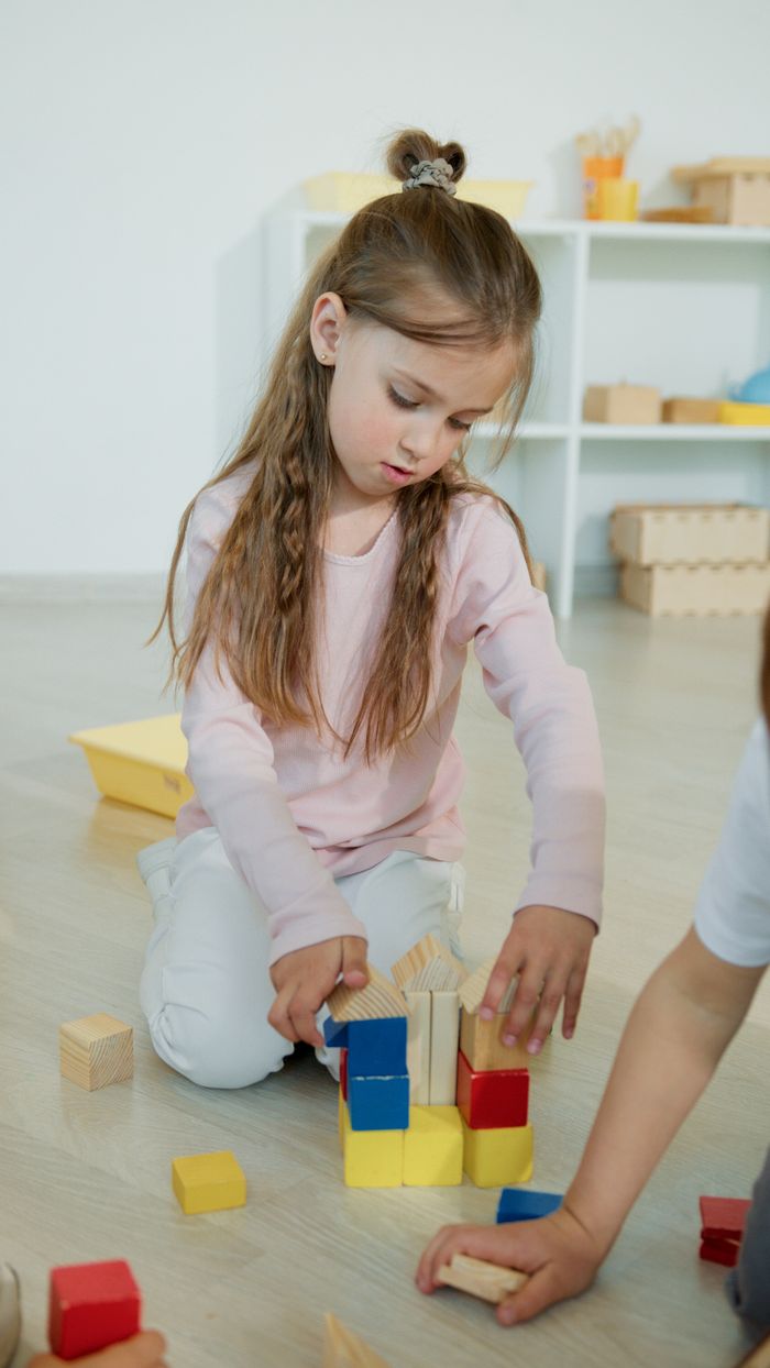 Young girl playing with colorful wooden blocks, fostering creativity and learning in a kindergarten setting.